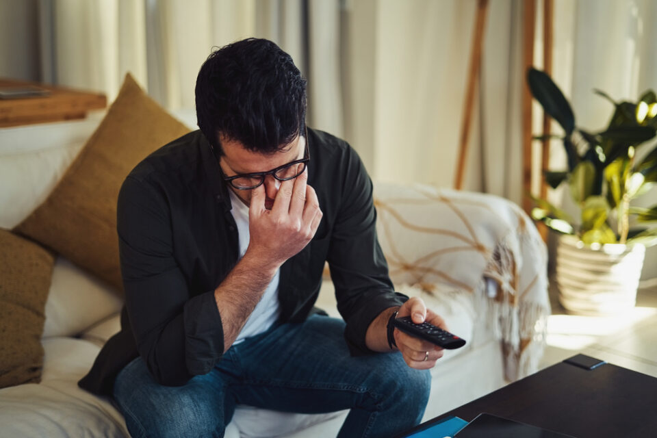 A man looking stressed while holding a remote control.