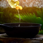 Oil being poured into a black frying pan outdoors.