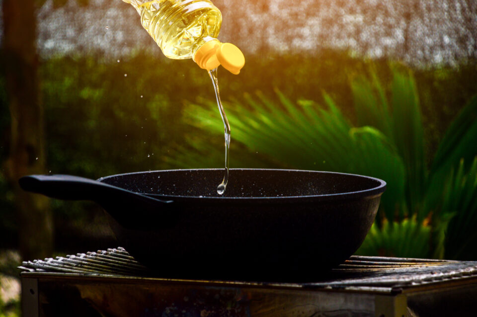 Oil being poured into a black frying pan outdoors.