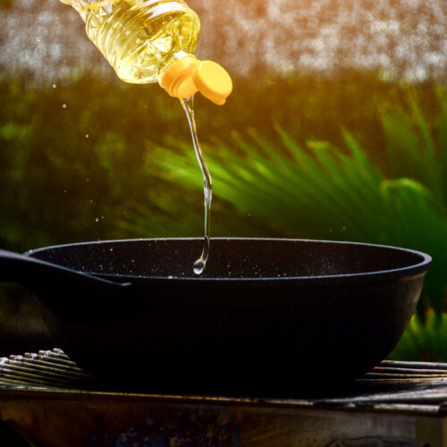 Oil being poured into a black frying pan outdoors.