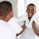 Man smiling at himself in the mirror with a towel around his neck.