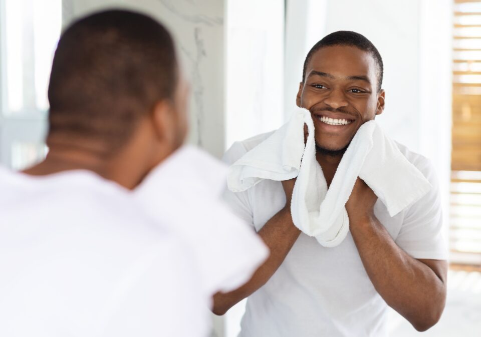 Man smiling at himself in the mirror with a towel around his neck.