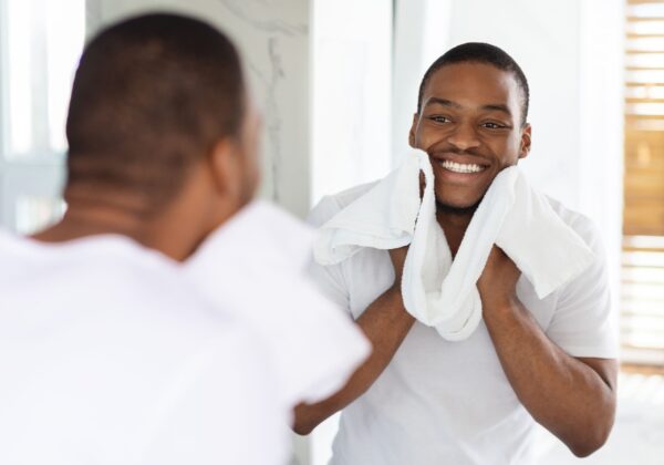 Man smiling at himself in the mirror with a towel around his neck.