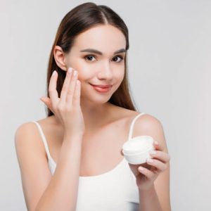 Young woman applying face cream with a smile.