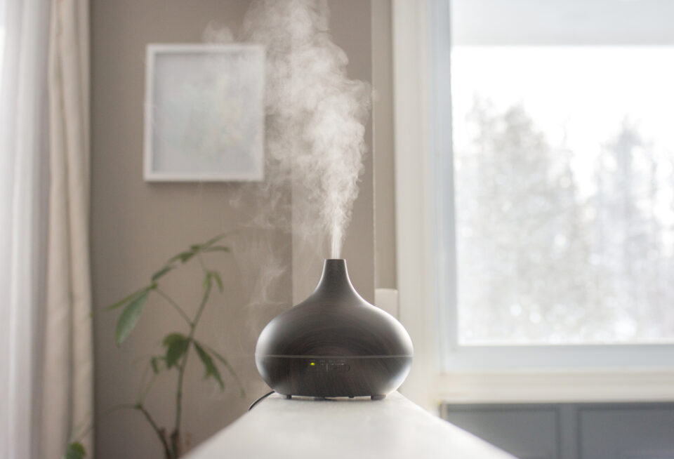 A sleek black essential oil diffuser releasing mist on a white surface.