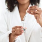 Person using a dropper to add liquid into a clear glass of water.