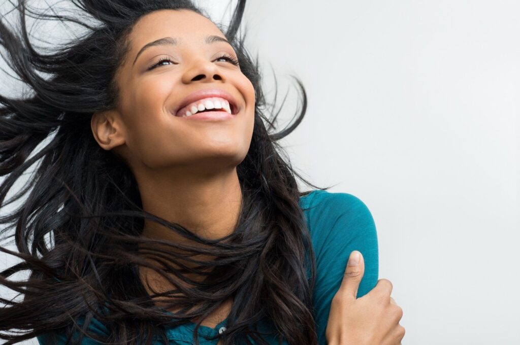 Joyful woman smiling with wind-blown hair against a light background.