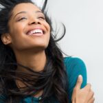 Joyful woman smiling with wind-blown hair against a light background.