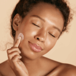 Woman gently applying cream to her cheek with eyes closed.
