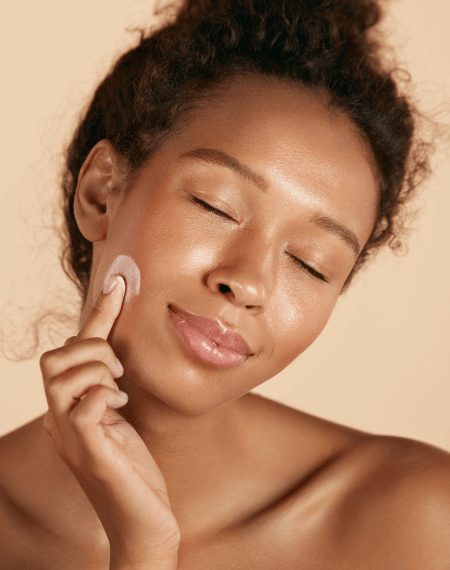 Woman gently applying cream to her cheek with eyes closed. Woman gently applying cream to her cheek with eyes closed.