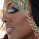 Close-up of a woman with artistic eye makeup and a plant near her face.
